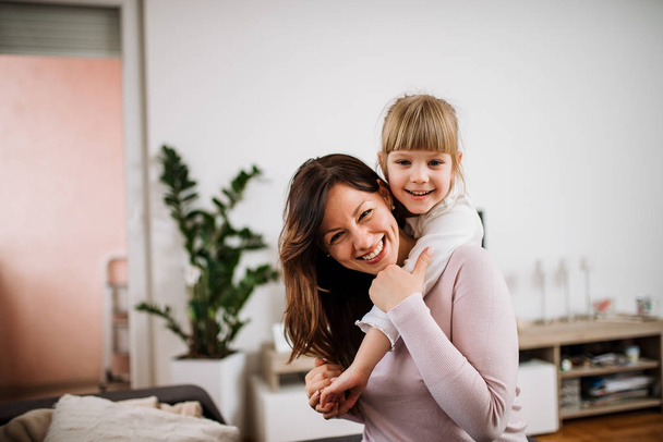Portrait of happy mother piggybacking daughter at home - Фото, изображение