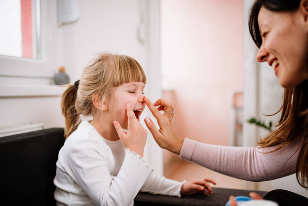 Smiling mother applying cream on face of little daughter  - Foto, Bild