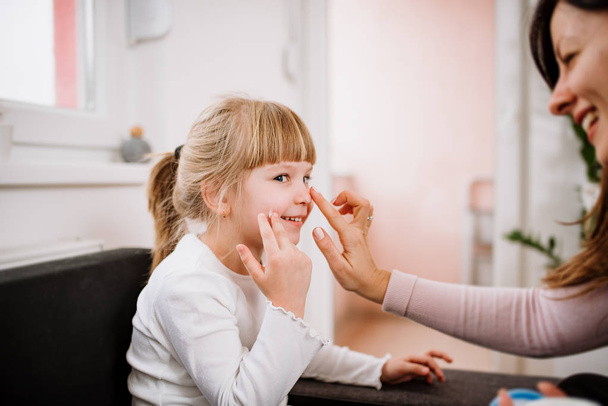 Smiling mother applying cream on face of little daughter  - Fotografie, Obrázek