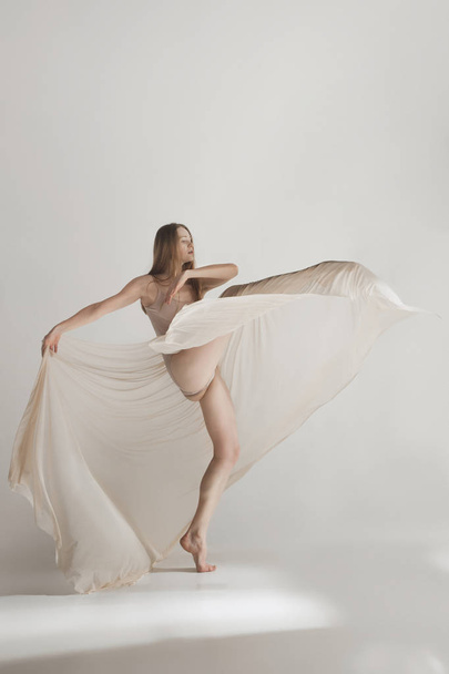 Young beautiful dancer in beige swimsuit dancing on gray background - Фото, зображення