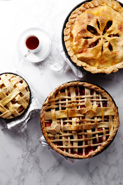 apple with strawberry and raspberry cooked pies with lattice and leaves and tea on white marble table  - Fotó, kép