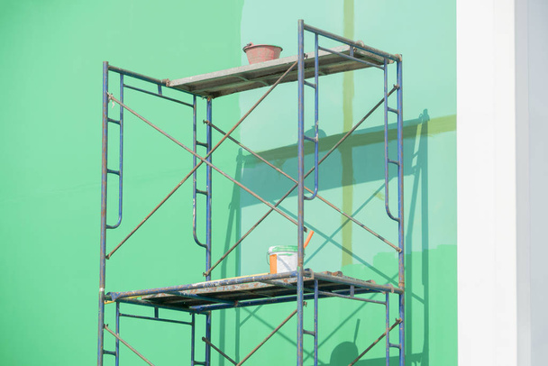 Scaffolding iron with green wall and paint bucket. - Foto, afbeelding