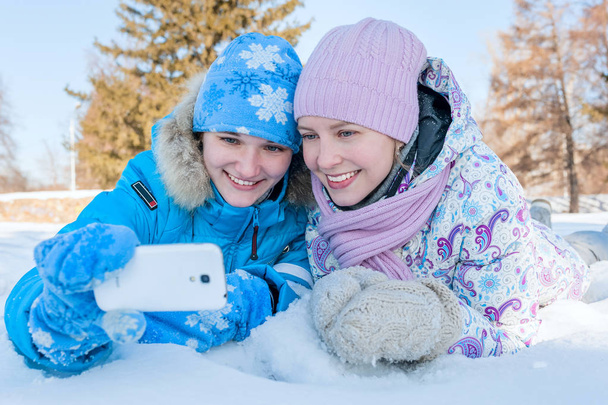 Selfie. Two young happy smiling girl lying on the snow in winter park. Outdoor portrait - Фото, зображення