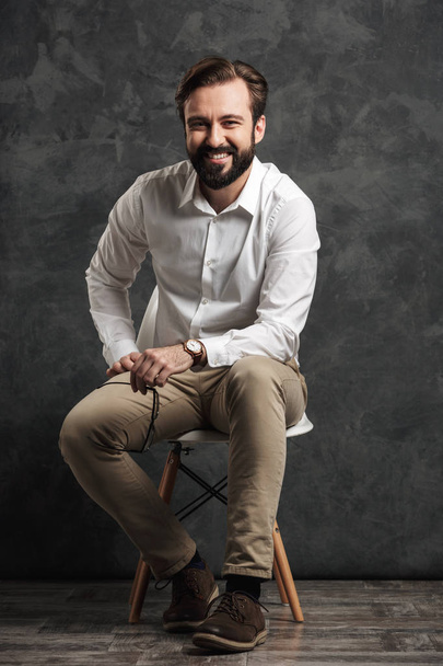 Cheerful bearded businessman sitting over grey wall - Fotó, kép