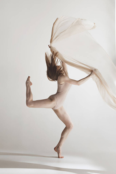 Young beautiful dancer in beige swimsuit dancing on gray background - Fotó, kép