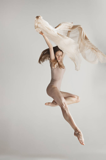 Young beautiful dancer in beige swimsuit dancing on gray background - Foto, Bild