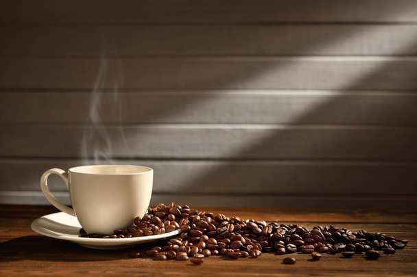 Šálek kávy s kouřem a káva fazole na dřevěné pozadí - Fotografie, Obrázek