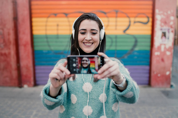 Beautiful woman listening to music with headphones and taking a selfie in the street - Foto, imagen