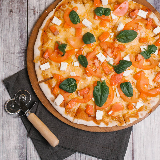 Pizza con salmón, feta, hojas de albahaca, tomates y mozzarella servidos en plato de pizza con cortador de pizza y servilleta verde oscuro
 - Foto, Imagen