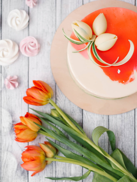 Food composition of white and red decorated cake with red tulips, meringues and wooden planks background - Foto, Bild