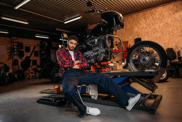 trabajador de la estación de reparación de bicicletas sentado delante de la motocicleta en el garaje
 - Foto, Imagen