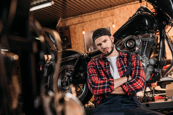 handsome bike repair station worker sitting in front of motorcycle - Фото, зображення