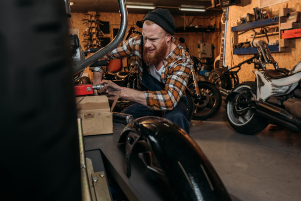 emotionele fiets repareren station werknemer trying voor positiebepaling fiets bij garage - Foto, afbeelding