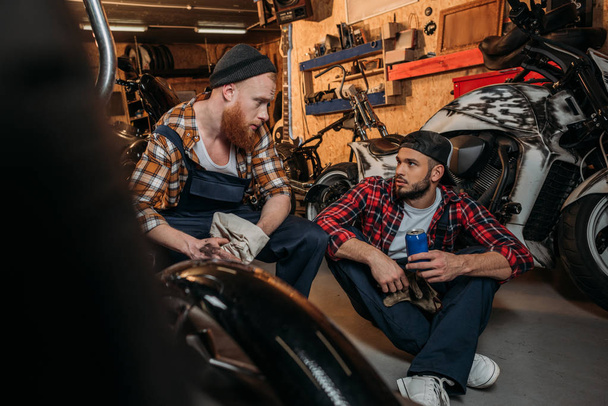 handsome mechanics having break in work at garage and chatting - Photo, Image