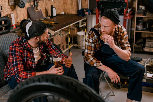 Mechaniker trinken Bier und essen in der Garage - Foto, Bild