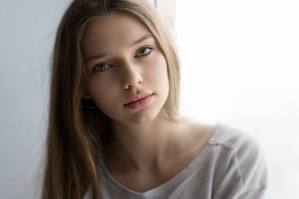 attractive teenager looking at camera while sitting near window  - Foto, Imagen