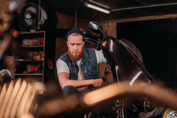 portrait of handsome young man on bike at garage - Photo, image