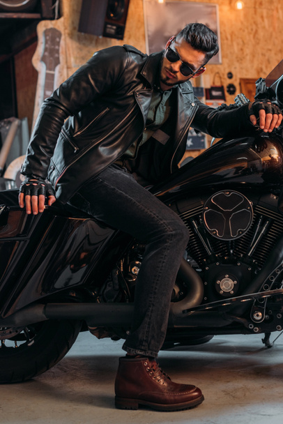 csinos, fiatal férfi ül a garázsban motorkerékpár elegáns ruházat - Fotó, kép