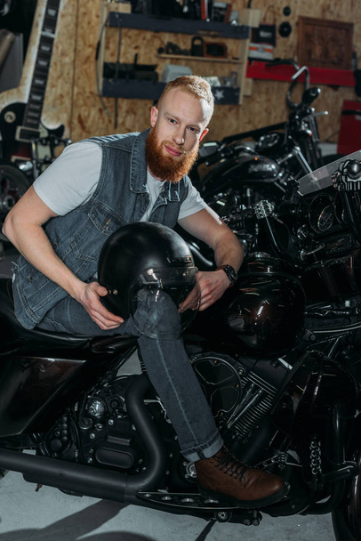 jeune homme assis sur une moto avec casque au garage
 - Photo, image