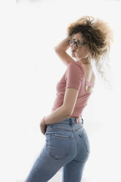 Woman with curly hair posing in t-shirt and jeans on white background - Фото, зображення