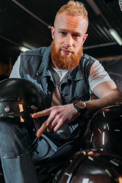 handsome young man sitting on bike with helmet at garage - 写真・画像