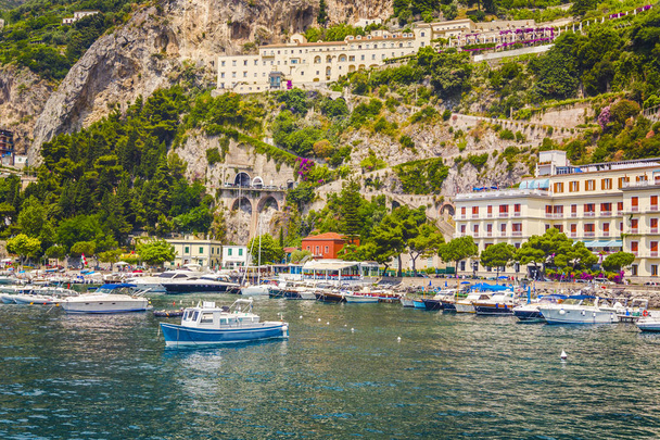 Vista desde el mar sobre la hermosa arquitectura de la ciudad de Amolphi y una pequeña bahía con barcos blancos y yates en la famosa costa de Amalfi con Golfo de Salerno, Campania, Italia
 - Foto, Imagen