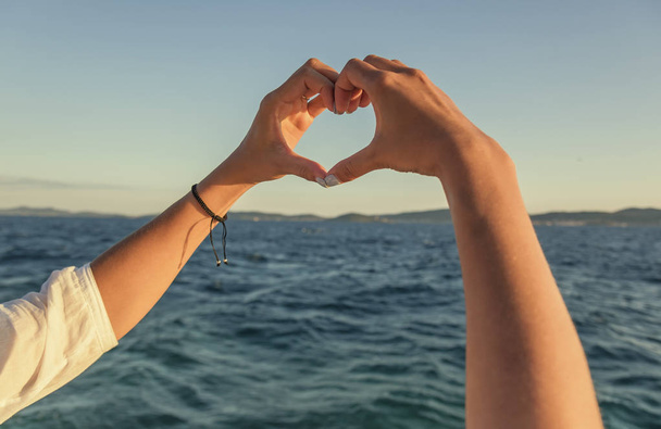 Τα χέρια σε σχήμα καρδιάς, το φόντο της θάλασσας. - Φωτογραφία, εικόνα
