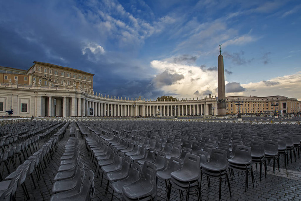 Vista grandangolare delle sedie vuote in Piazza San Pietro prima dell'ingresso alla messa pubblica sullo sfondo drammatico del cielo, Città del Vaticano, Italia
 - Foto, immagini