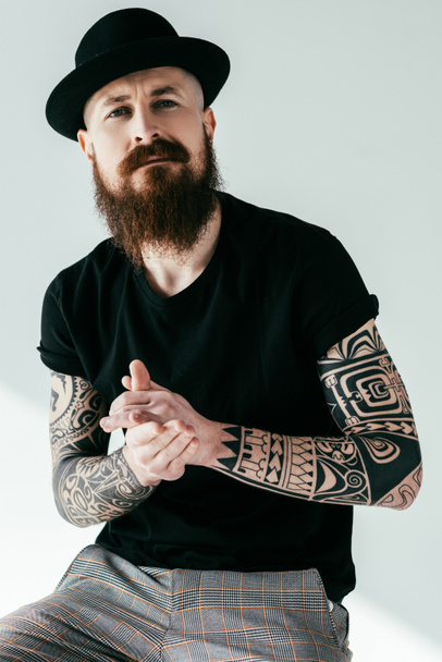 handsome bearded tattooed man in hat looking at camera on white - Photo, Image