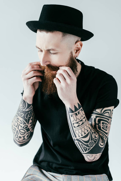 handsome bearded tattooed man twisting mustache isolated on white - Fotó, kép