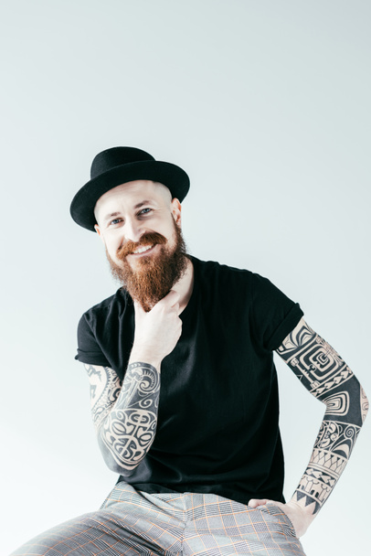 smiling tattooed man touching beard and looking at camera isolated on white - Fotoğraf, Görsel