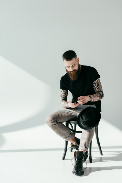 stylish bearded tattooed man using smartphone on white - Фото, зображення