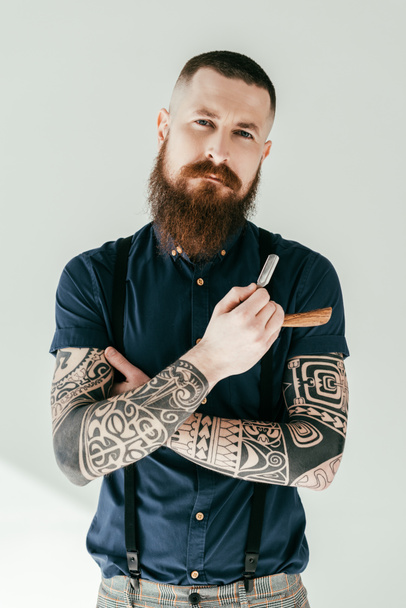 handsome tattooed man holding razor and looking at camera - Photo, Image