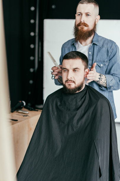 barber looking at client haircut in mirror at barbershop - Foto, afbeelding