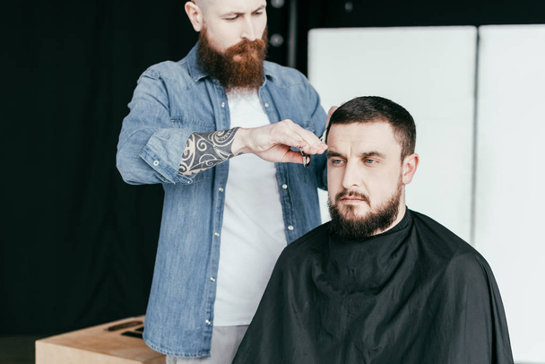 barber cutting serious customer hair at barbershop - Foto, imagen