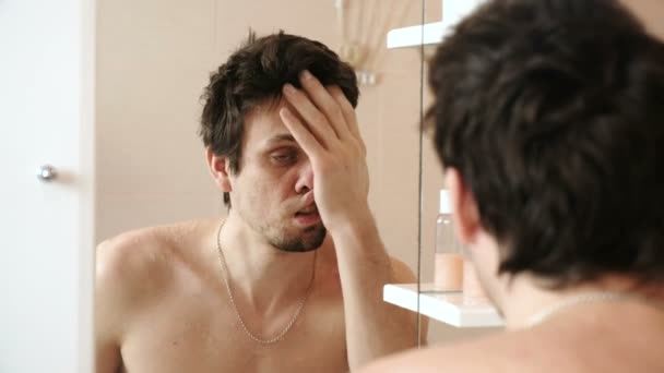 Tired man who has just woken up llooking at his reflection in the mirror and rubs his face with his hand. - Filmagem, Vídeo
