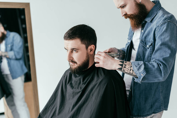 serious barber shaving client hair at barbershop isolated on white - Valokuva, kuva