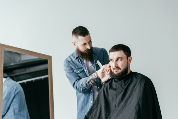 bearded barber shaving customer hair at barbershop isolated on white - Фото, изображение