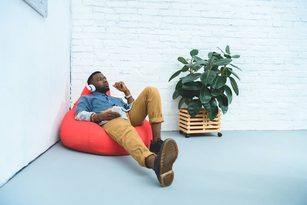 African american man listening to music in earphones while sitting in bean bag - Fotó, kép