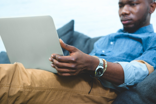 African american man sitting on sofa and working on laptop - Foto, Imagem