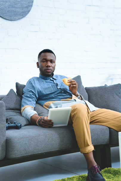 Uomo afroamericano in possesso di tablet e mangiare hamburger
 - Foto, immagini