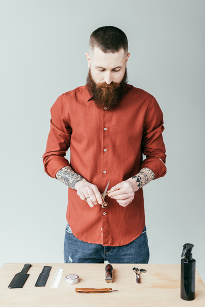 handsome barber holding scissors and looking at equipment isolated on white - Valokuva, kuva