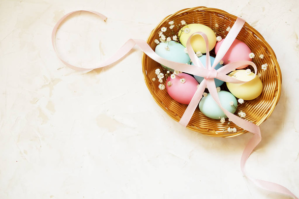 Tradycyjnego szablonu karty Wielkanoc z pastelowe kolory malowane ekologiczne jaja w wiklinowym koszu z siana i dekoracyjne kwiaty. - Zdjęcie, obraz