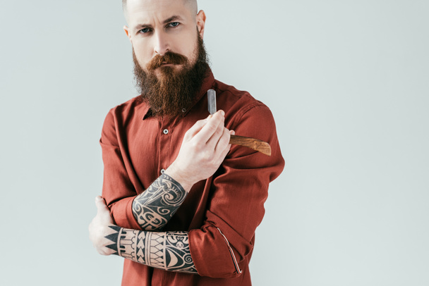 bearded serious barber holding razor isolated on white - Foto, afbeelding