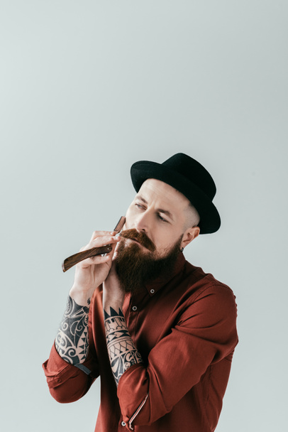 bearded tattooed man shaving beard with razor isolated on white - Photo, Image
