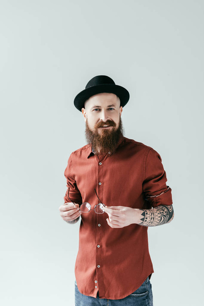 smiling bearded man holding glasses and looking at camera isolated on white - Photo, Image