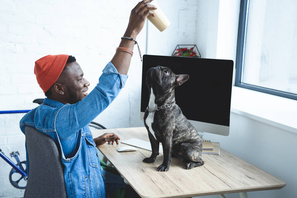 Handsome african american man playing with dog on computer table - 写真・画像