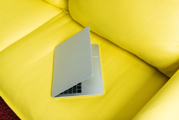 Portátil semicerrado en sofá de cuero amarillo, concepción minimalista
 - Foto, Imagen