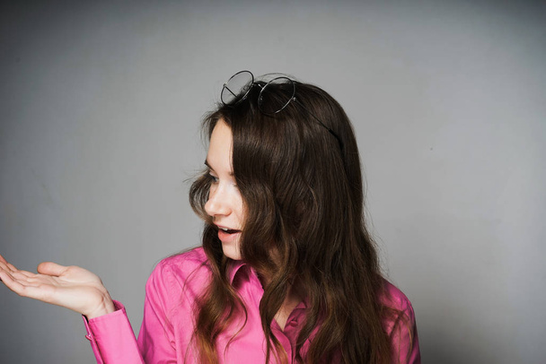 beautiful young woman in a pink shirt, with long hair, shows something by hand - Zdjęcie, obraz