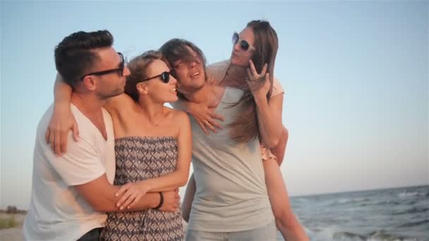 Ritratto di quattro amici che si divertono insieme sulla spiaggia durante il tempo ventoso e si godono il tramonto
. - Filmati, video